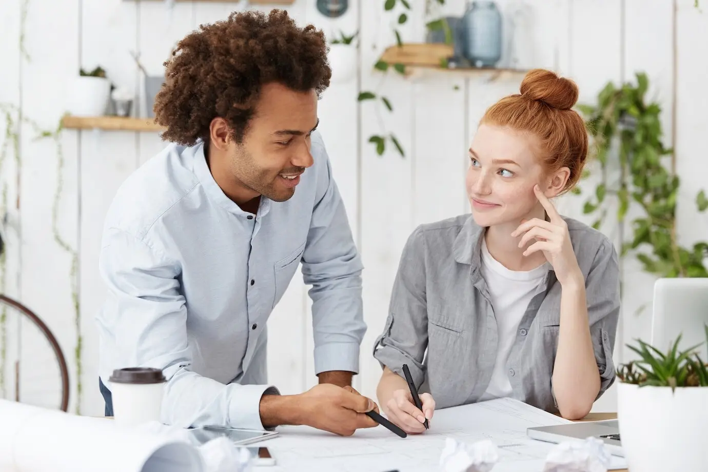 Two creative coworkers, forming a united international team, sit at a desk with blueprints.