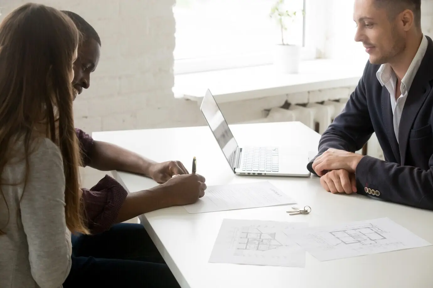 An interracial couple is signing a mortgage investment contract during a meeting with a broker.